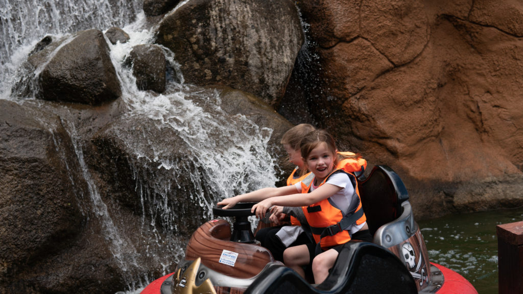 Children enjoying water ride with waterfall backdrop.