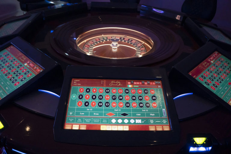 Close-up of a digital roulette table with screens in a dimly lit casino setting.