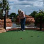 Person playing mini-golf outdoors on a sunny day with colourful balls.