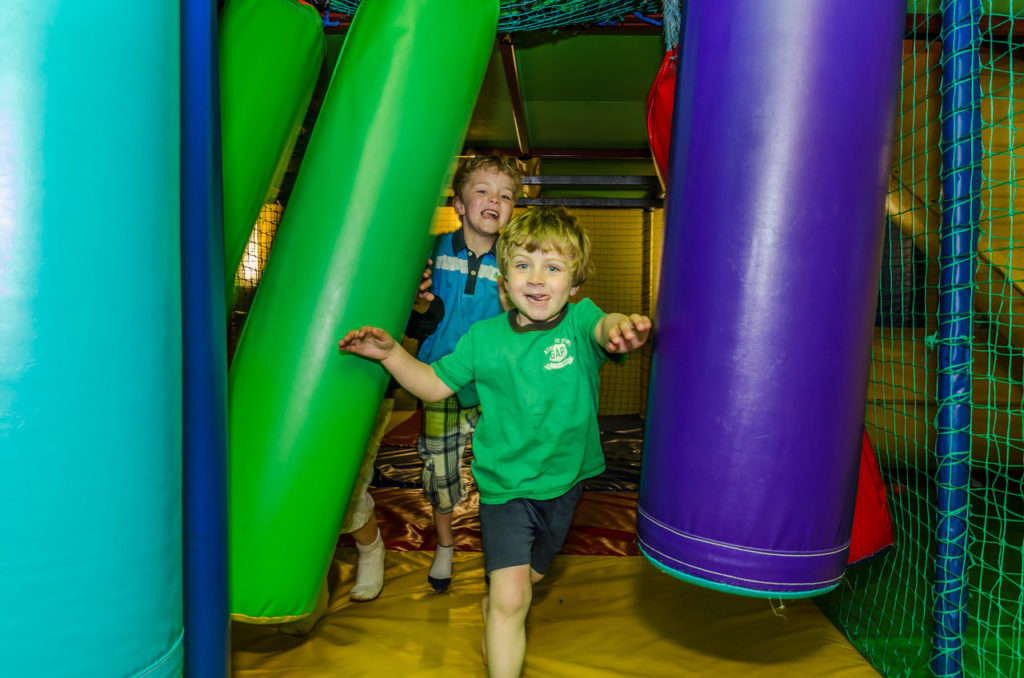 Children playing joyfully in a colourful indoor soft play area.