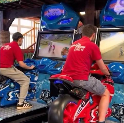 Men playing motorcycle arcade racing game indoors.