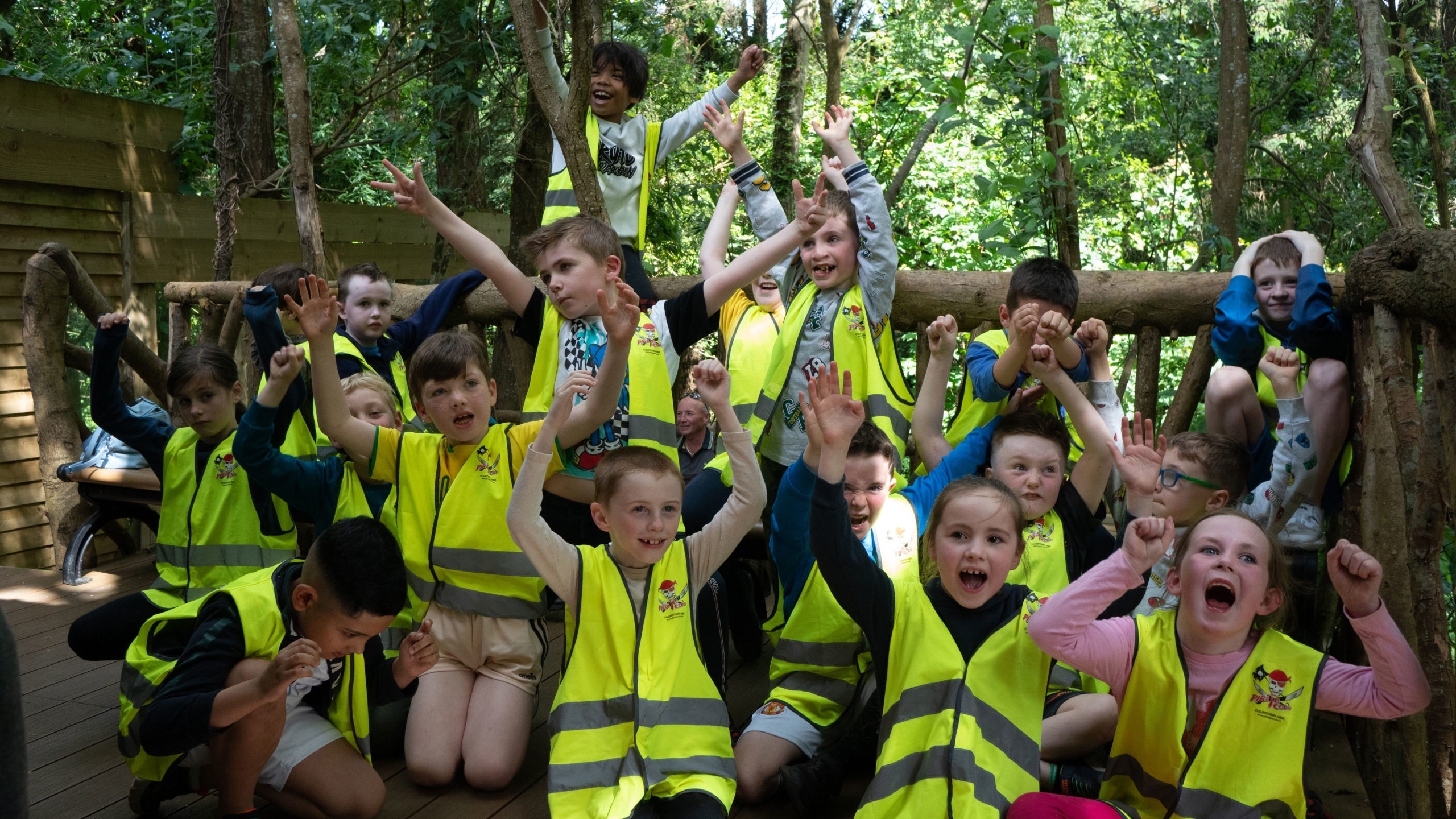 Children cheering in high-vis vests during a woodland adventure.