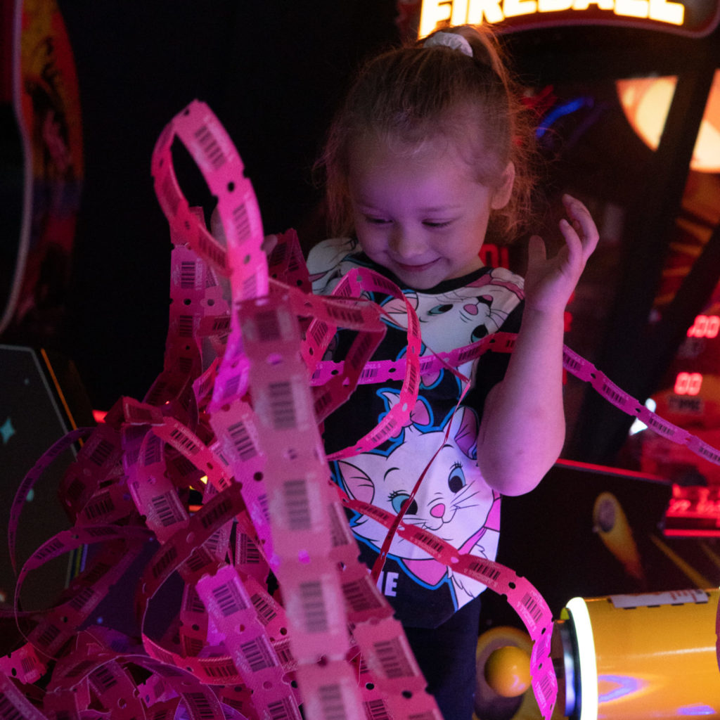 Young child smiling with arcade tickets in game centre.