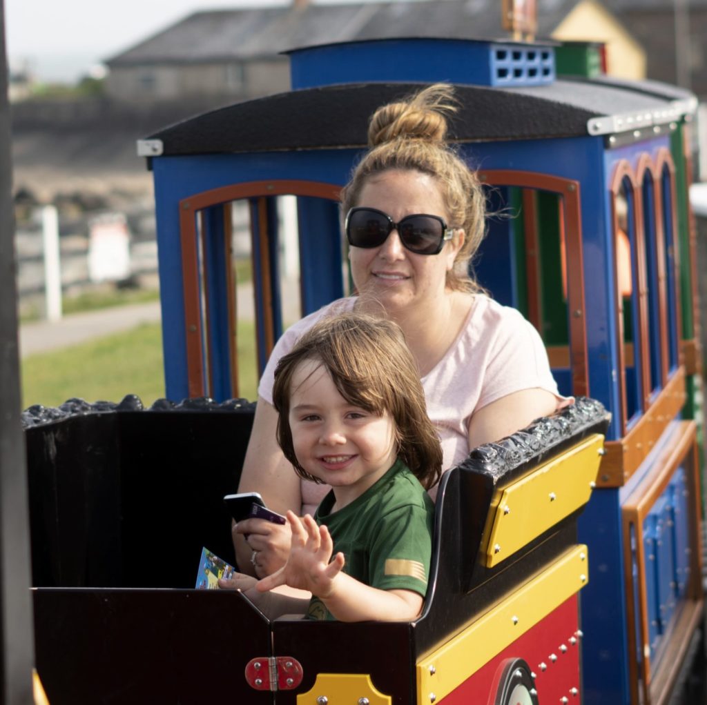 Child enjoying a mini train ride with an adult on a sunny day.