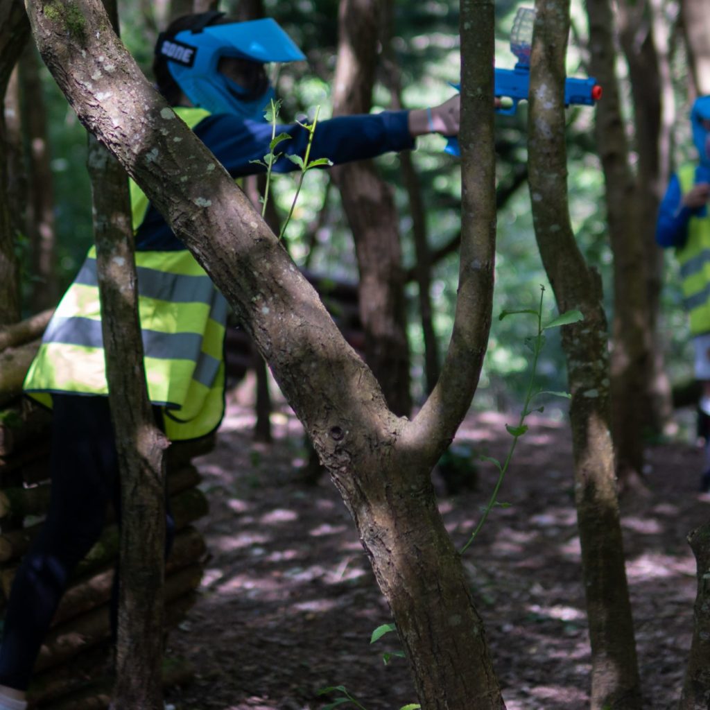 Person in high-vis vest playing laser tag in wooded area.