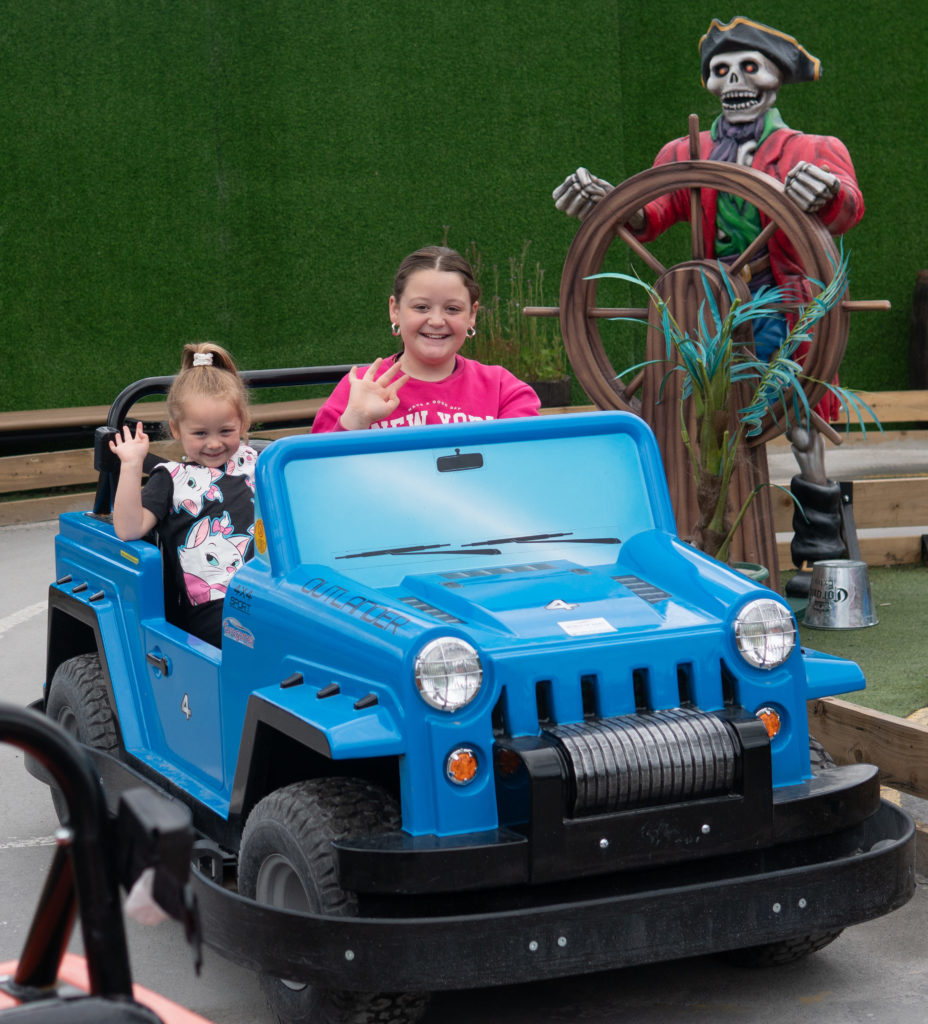 Kids enjoy bumper car ride at amusement park, with pirate statue in background.
