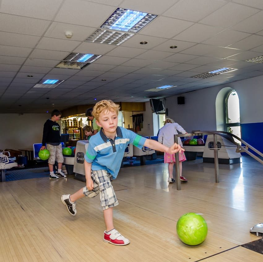 Child bowling indoors with green ball on wooden lane.