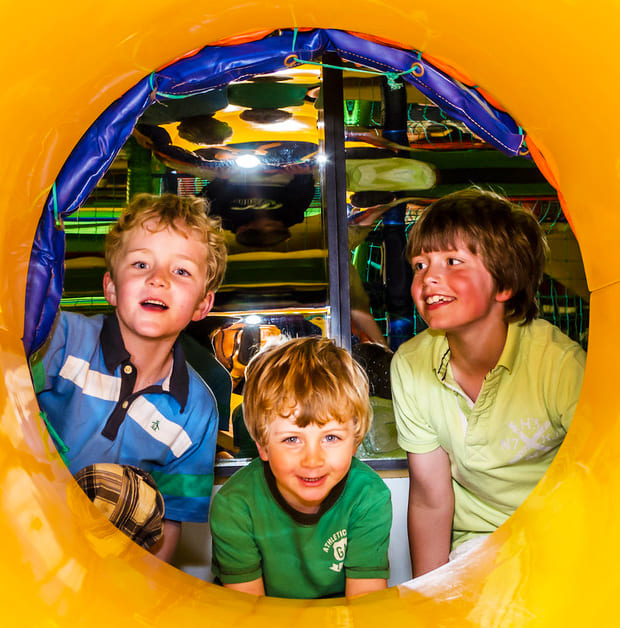 Children playing in a colourful indoor playground tunnel.