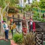 People playing mini golf in pirate costumes, surrounded by exotic plants.
