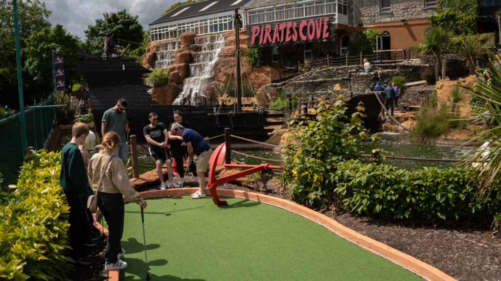 Mini golf at Pirate’s Cove adventure park with a waterfall backdrop and greenery.