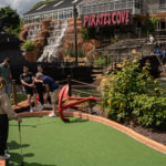 Mini golf at Pirate’s Cove adventure park with a waterfall backdrop and greenery.