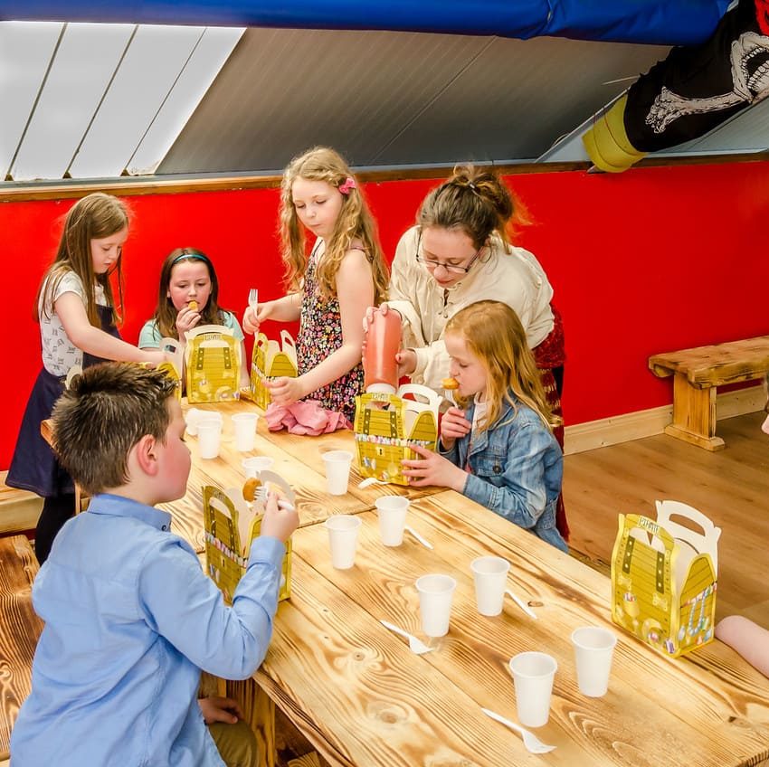 Children having a birthday party meal with snacks and drinks at a colourful venue.