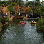 Boats on a lush green amusement park water ride with scenic surroundings.