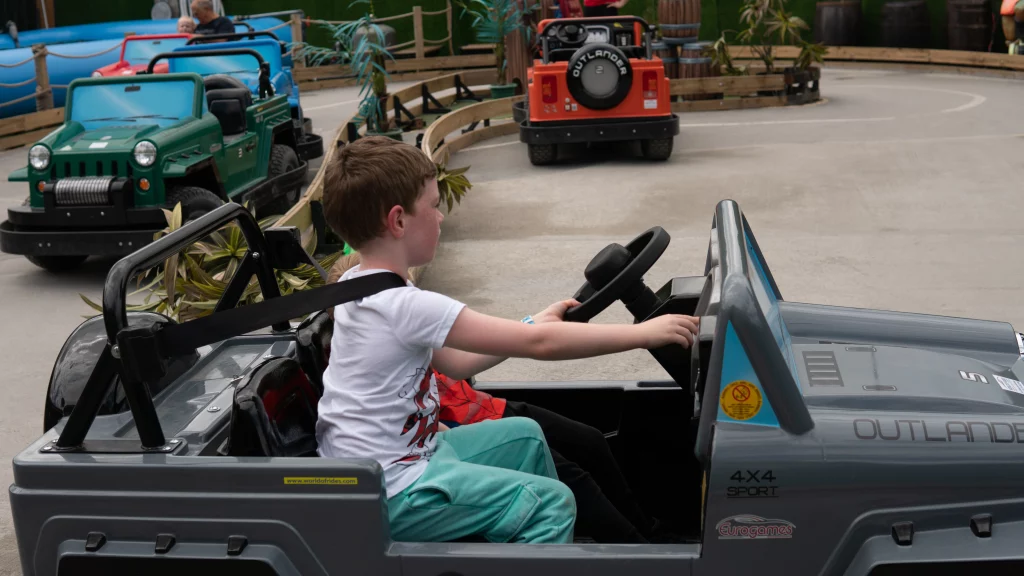 Young child driving a toy jeep on a go-kart track.