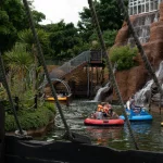 Boats in a theme park water ride near a waterfall on a cloudy day.