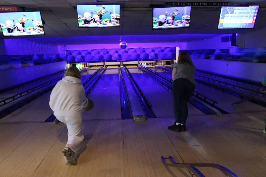 Two people bowling in a dimly lit alley with neon screens.