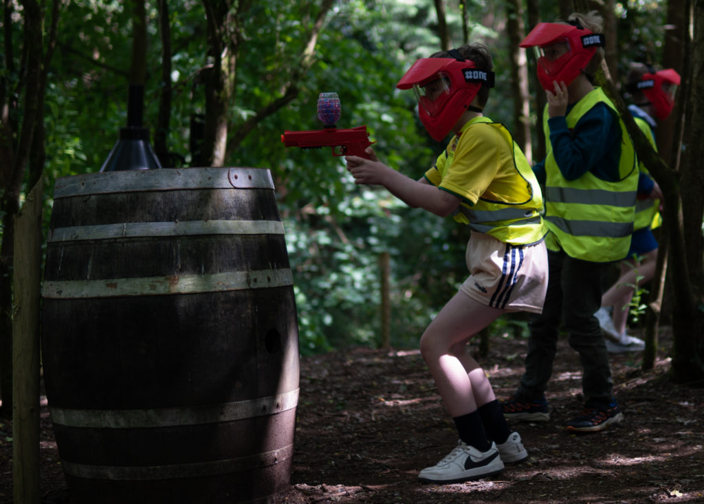 Children playing paintball in the woods wearing safety masks.