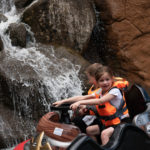 Children enjoying a log flume ride with waterfall backdrop.