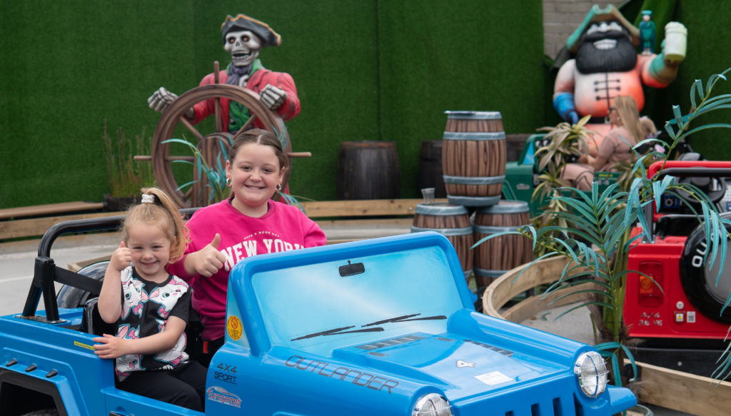 Children ride in toy car at pirate-themed amusement park.