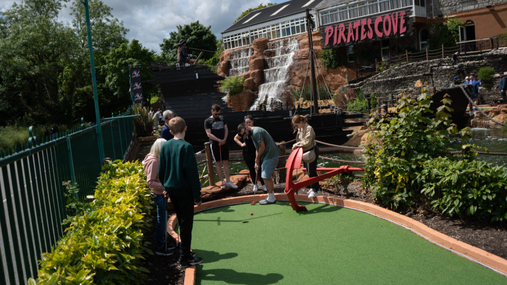 Group playing mini golf at Pirates Cove with waterfall and ship backdrop.