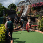 Group playing mini golf at Pirates Cove with waterfall and ship backdrop.