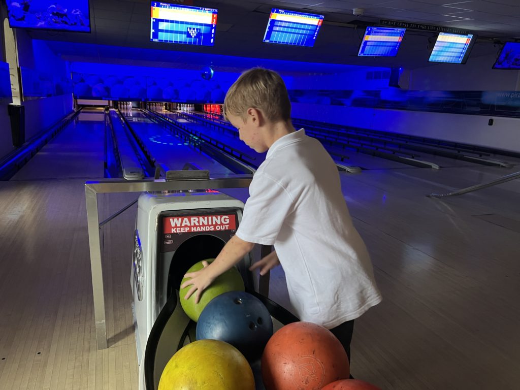 Boy selecting bowling ball at a vibrant, neon-lit alley.